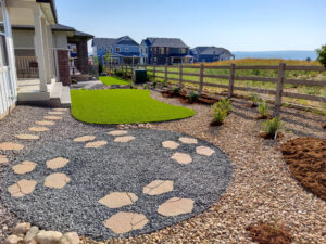 Backyard with stone pathways, gravel and pebble ground cover, small plants, and wooden fence.