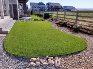 Residential backyard with artificial grass, decorative rocks, garden bed, and wooden fence.